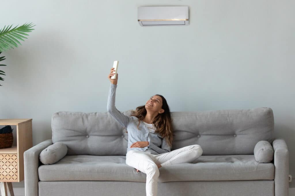 Smiling woman relaxing on couch, using air conditioner remote controller