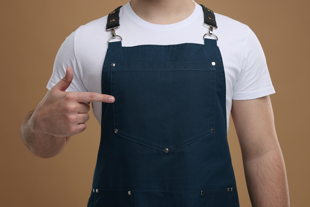 Man,Pointing,At,Kitchen,Apron,On,Brown,Background,,Closeup.,Mockup